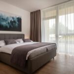 Moderná spálňa s manželskou posteľou, elegantným nábytkom a veľkými presklenými dverami v apartmáne DaSus Luxury Tále.