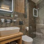 Elegantná kúpeľňa so sprchovým kútom, umývadlom a kamenným obkladom v apartmáne Sosana