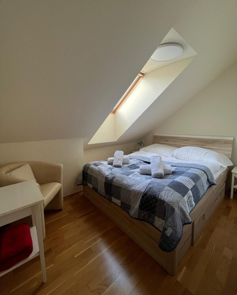 Podkrovná spálňa vo Villa S. Gallen s manželskou posteľou, strešným oknom a útulným posedením.